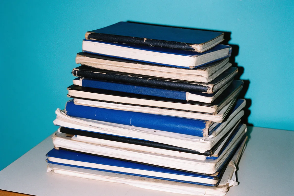 A tall stack of worn sketchbooks